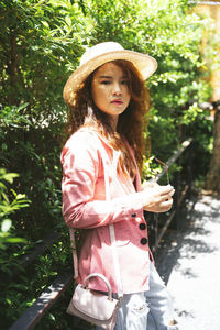 Portrait of young woman in hat standing against plants