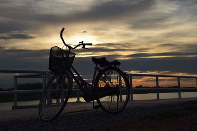 Bicycle by sea against sky during sunset