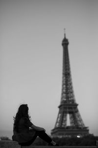 Side view of woman sitting on retaining wall against eiffel tower