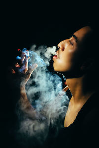 Young man looking away while smoking against black background
