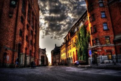 Road leading towards buildings against cloudy sky