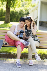 Happy couple looking photos on camera while sitting on bench in park