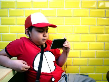 Boy playing with mobile phone against yellow wall