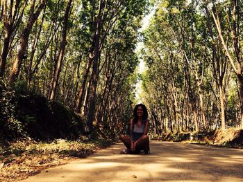 Happy woman sitting on dirt road amidst trees in forest