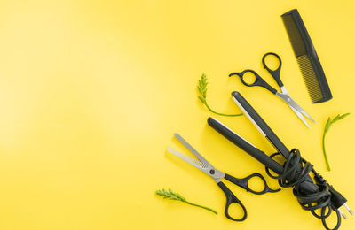 Scissors and other hairdresser's accessories on yellow background, flat lay. space for text