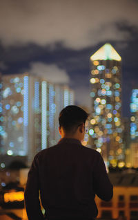 Rear view of man standing against illuminated city at night