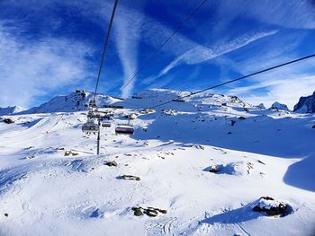 Ski lift over snow covered mountains against sky