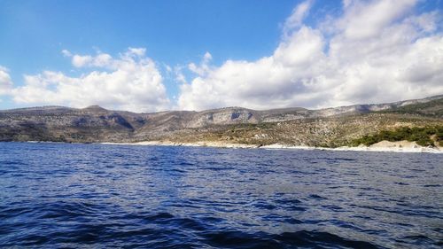 Scenic view of sea by mountain against sky