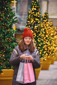 Woman wearing hat standing against illuminated christmas tree
