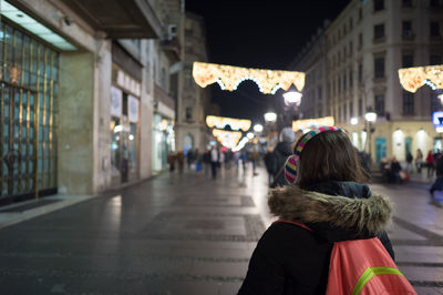 Rear view of woman listening music through headphones in city at night