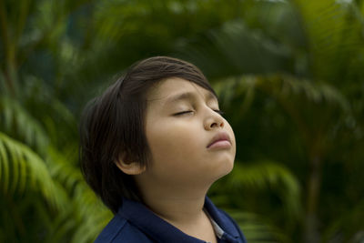 Close-up of boy with eyes closed against trees