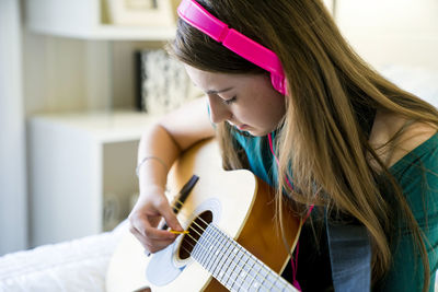 Teenage girl playing guitar in bedroom