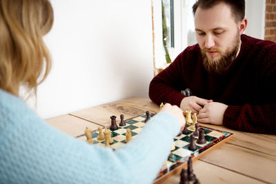 Young man and woman playing chess while sitting on table at home