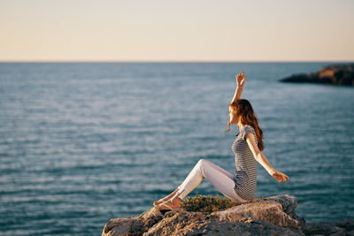 Woman on rock by sea against sky