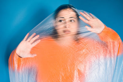 Woman covered in plastic standing against blue background