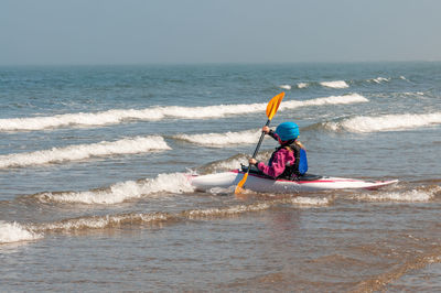 Young girl paddling kayak through surf out towards the sea on a sunny day