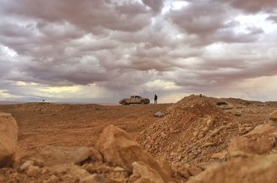 Person with car standing on land against cloudy sky