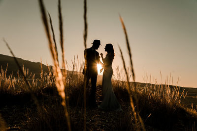 Silhouette couple standing on field against sky during sunset