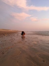 Teenage girl photographing at beach against sky during sunset