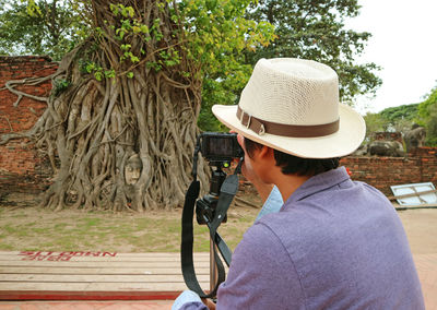 Visitor taking photos of ancient buddha statue's head trapped in bodhi tree, ayutthaya, thailand