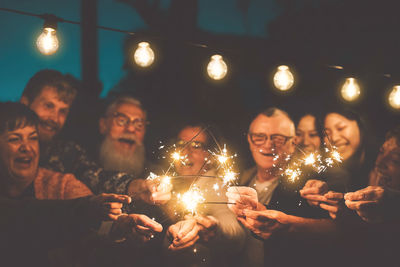 Men and women holding illuminated sparklers at night
