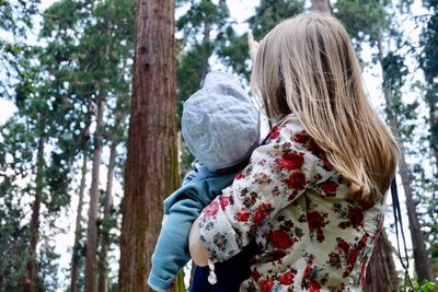 Rear view of woman walking on tree trunk in forest