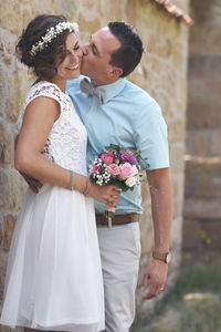 Groom kissing smiling bride against house