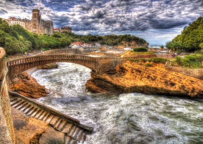 Arch bridge over river against cloudy sky