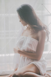 Close-up of young woman sitting by window curtain at home