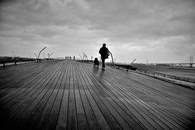 Full length of man with dog walking on boardwalk against sky