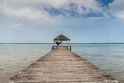 Wooden pier leading to calm sea against cloudy sky
