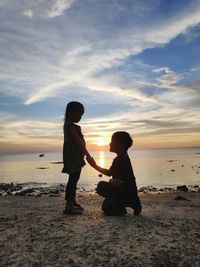 Boy proposing girl on shore at beach during sunset