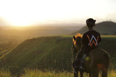 Rear view of man riding on field against sky during sunset