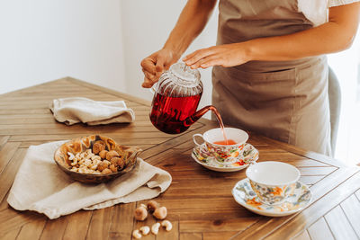 Midsection of woman pouring hibiscus tea in cups on table