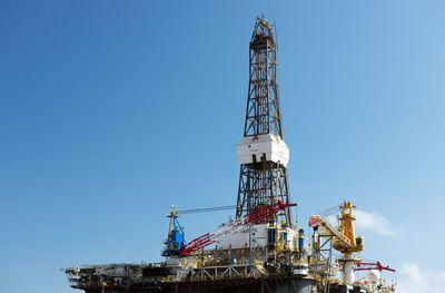 Low angle view of oil rig against blue sky