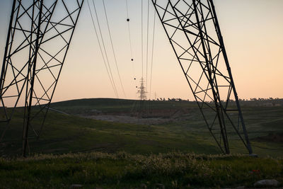 Electricity pylon on land against sky during sunset