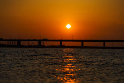 Silhouette bridge over sea against romantic sky at sunset