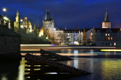 Illuminated buildings by river against sky at night