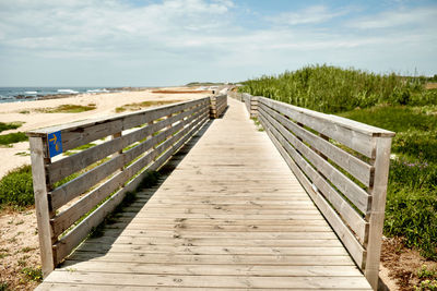 Boardwalk leading towards footbridge against sky