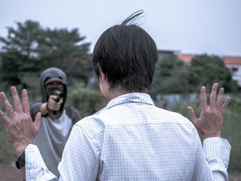 Man with arms raised standing in front of thief pointing gun at him