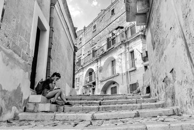 Woman sitting on steps against buildings in city