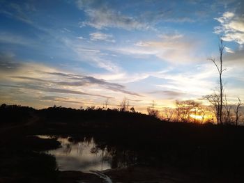 Silhouette trees by lake against sky during sunset