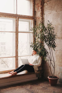 Woman sitting on potted plant by window