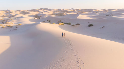 High angle view of couple walking on sand at desert against sky