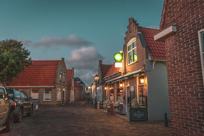 Illuminated street amidst buildings against sky at dusk