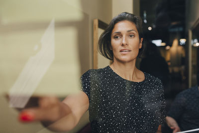 Mid adult businesswoman reading ideas on glass wall in office