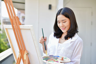 Young woman holding colorful palate by canvas 