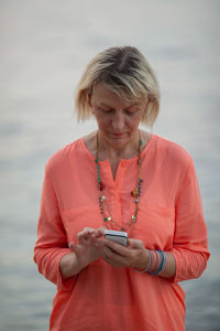 Mid adult woman using phone while standing on shore