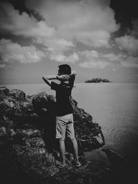 Man standing on rock by sea against sky