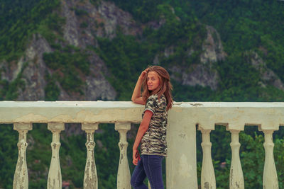 Portrait of young woman standing by railing against mountains